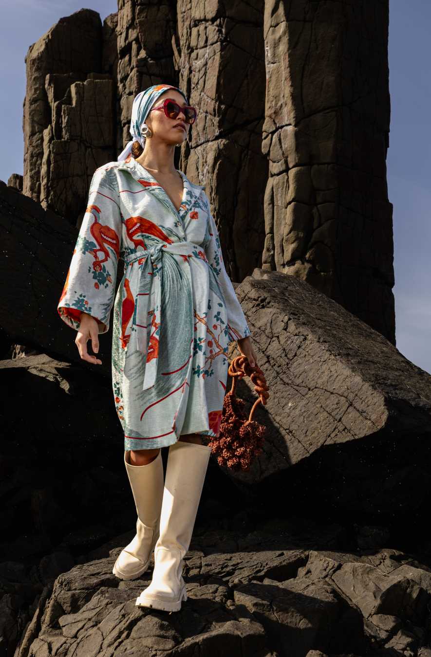 Outdoor editorial shot of model wearing floral dress and carrying the cream Ameba Mesh Bag against a rocky coastal setting in Peru.