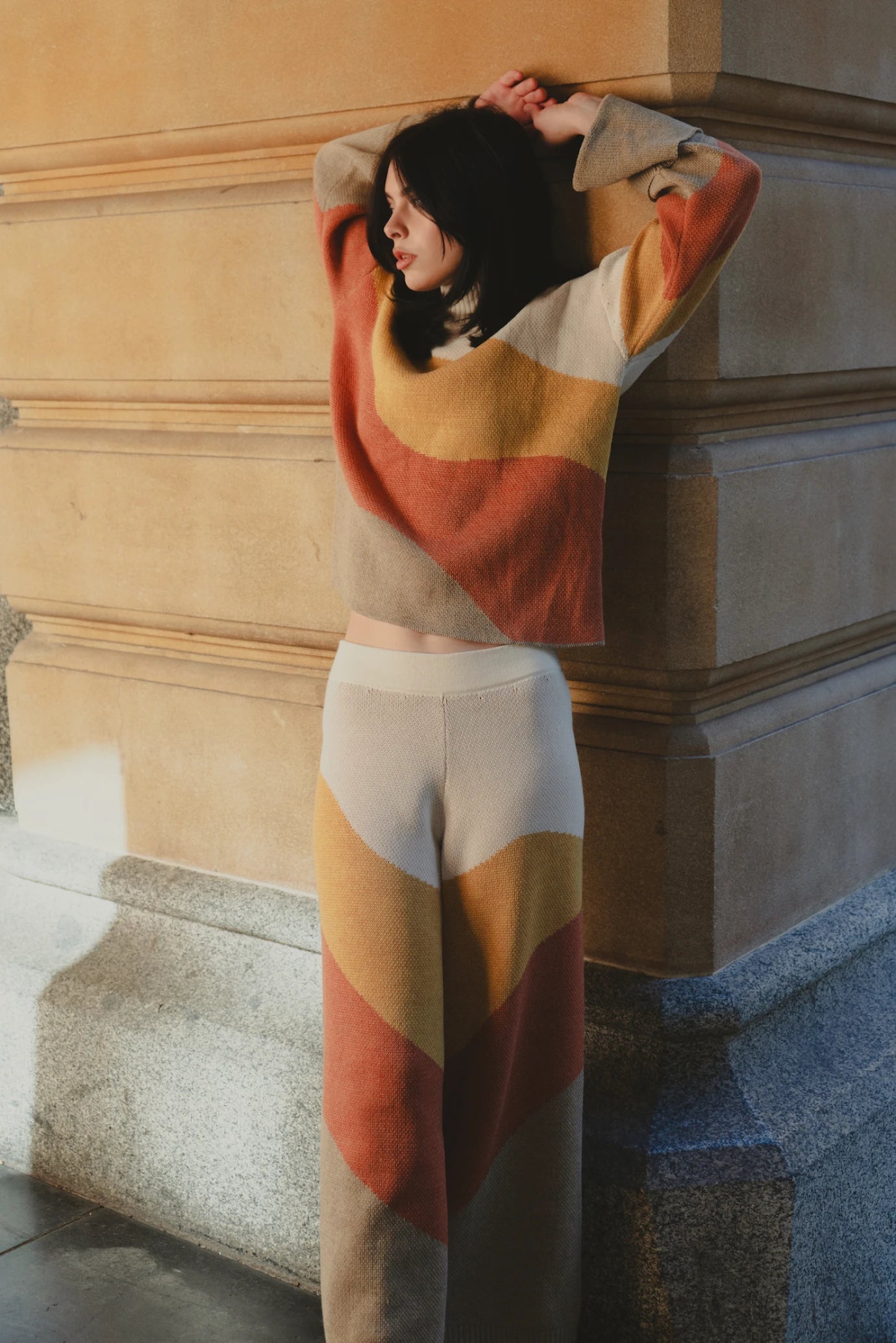 Model wearing the My Paloma colour block knit set, standing against a sandstone building in soft natural light, highlighting the luxurious drape and rich hues of the co-ord ensemble.