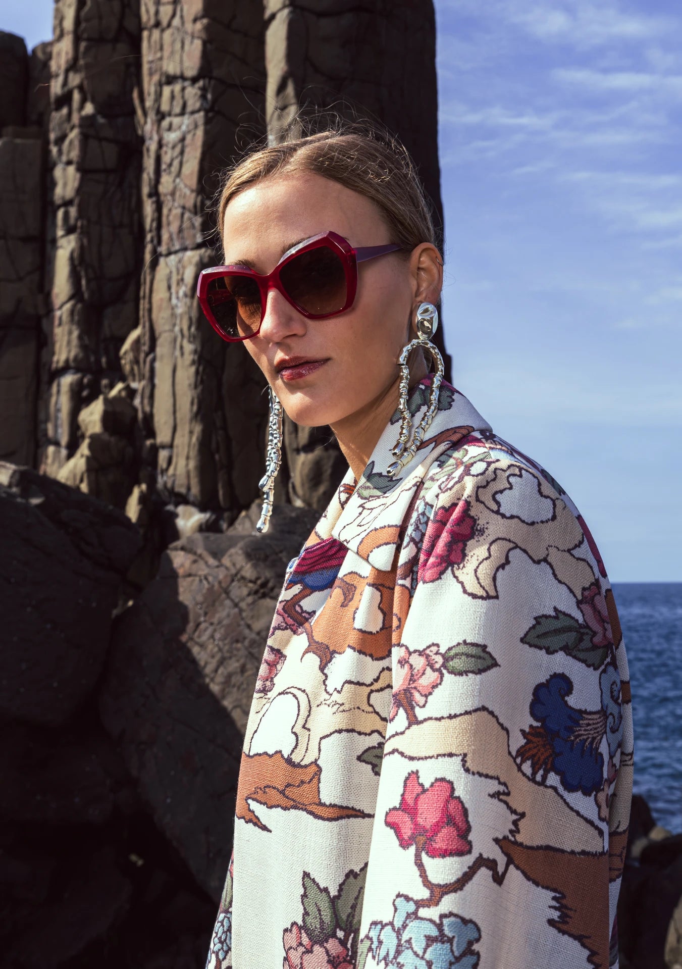 Model wearing Phoenix Kimono with peach and green bird motifs, photographed in Lisbon, Portugal – cultural craftsmanship by My Paloma. Big red sunglasses and Ornate silver earrings.