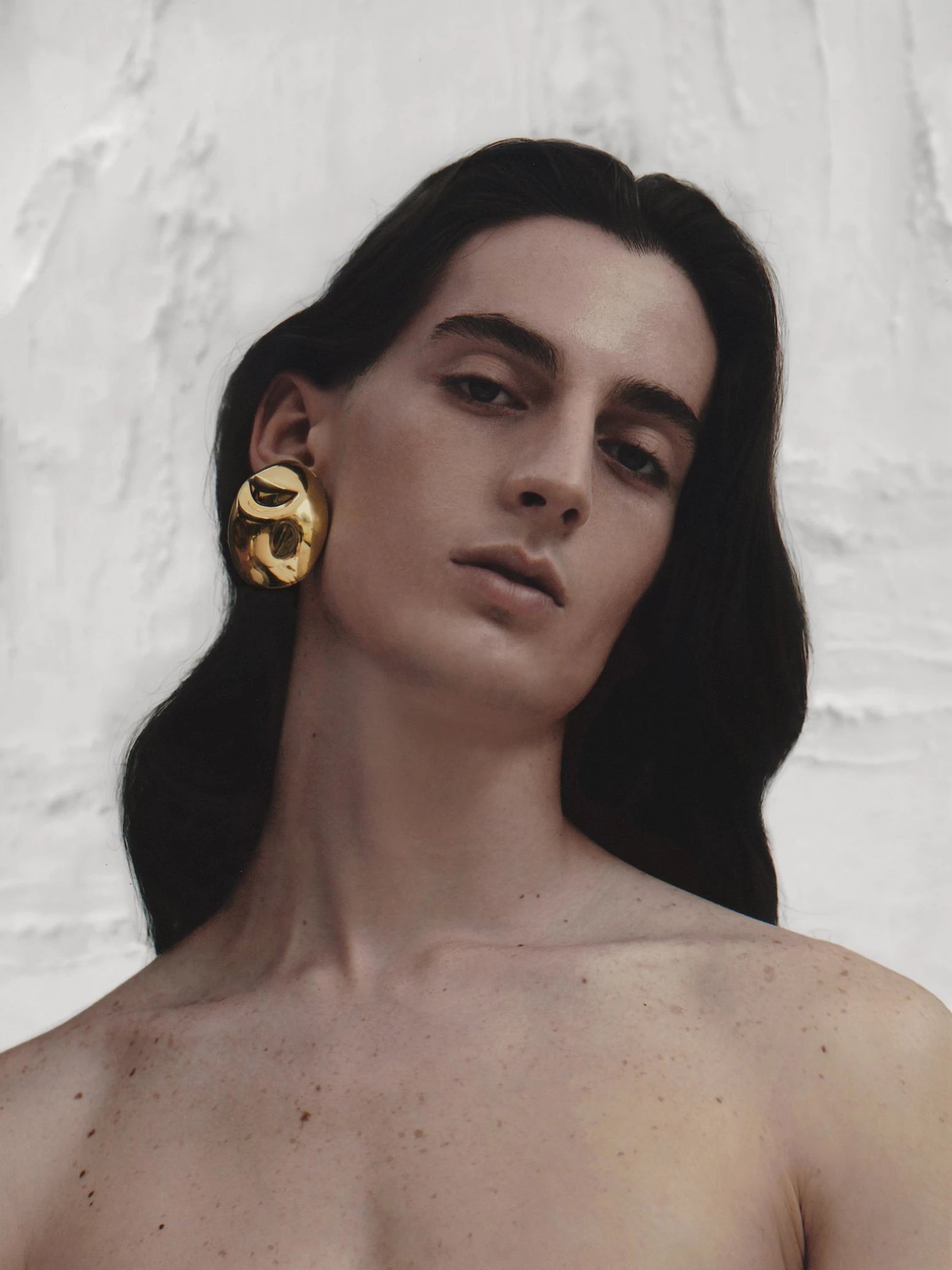 Profile shot of model with long dark hair showcasing statement gold sculptural earrings for a refined, gallery-inspired aesthetic.