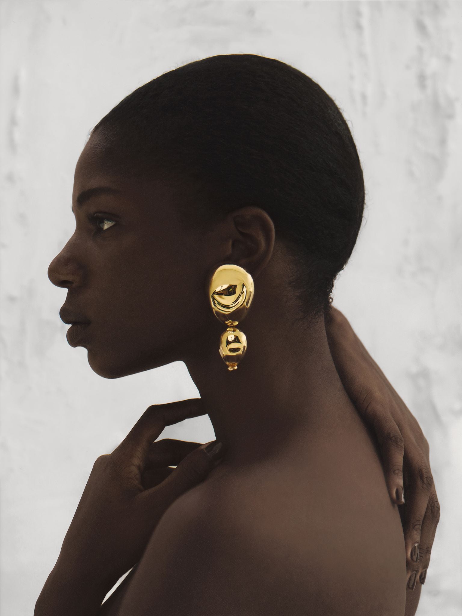Side profile of a model wearing gold drop earrings that catch the light, complementing her silhouette with modern elegance and warmth.